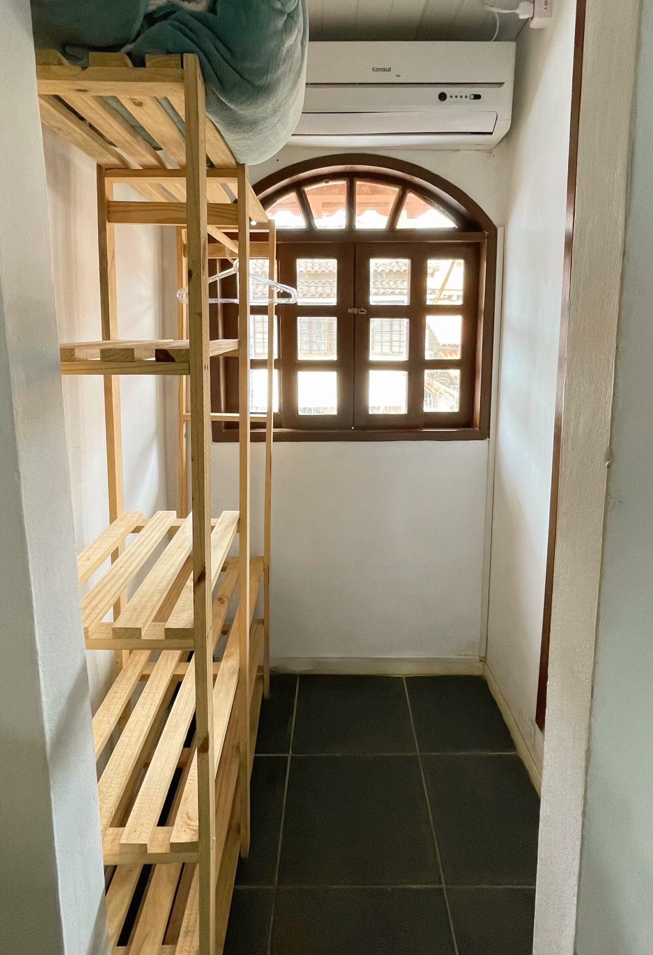 A small room with a wooden bunk bed, a window with a decorative grille, and an air conditioning unit above.