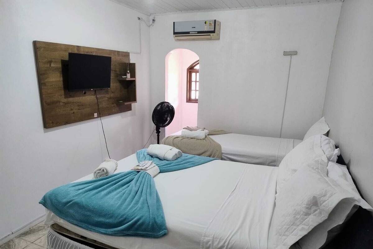 A room with two beds, a TV mounted on the wall, an air conditioner, and a fan.