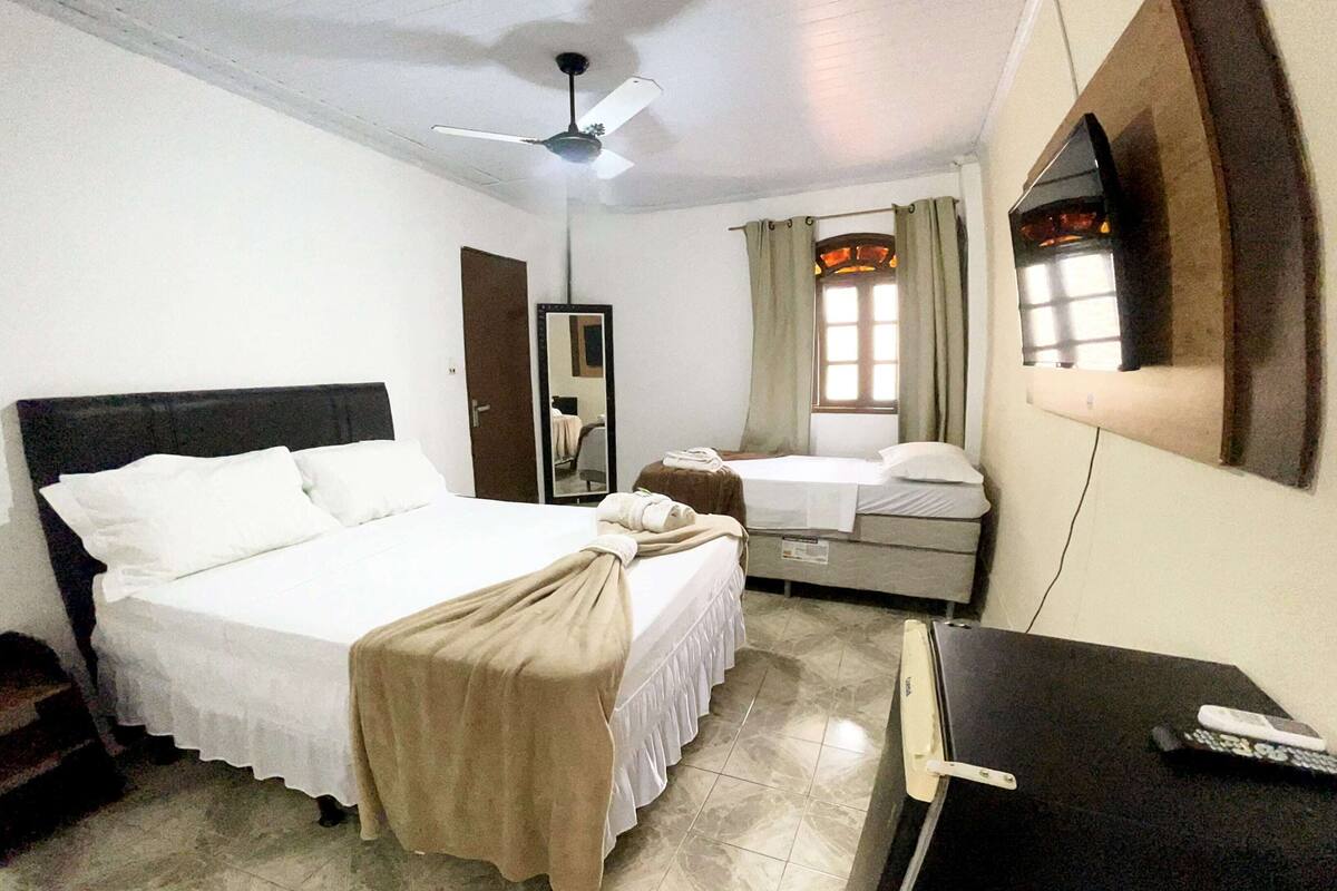 A hotel room with a bed, a desk, a chair, a mirror, and a window with curtains.