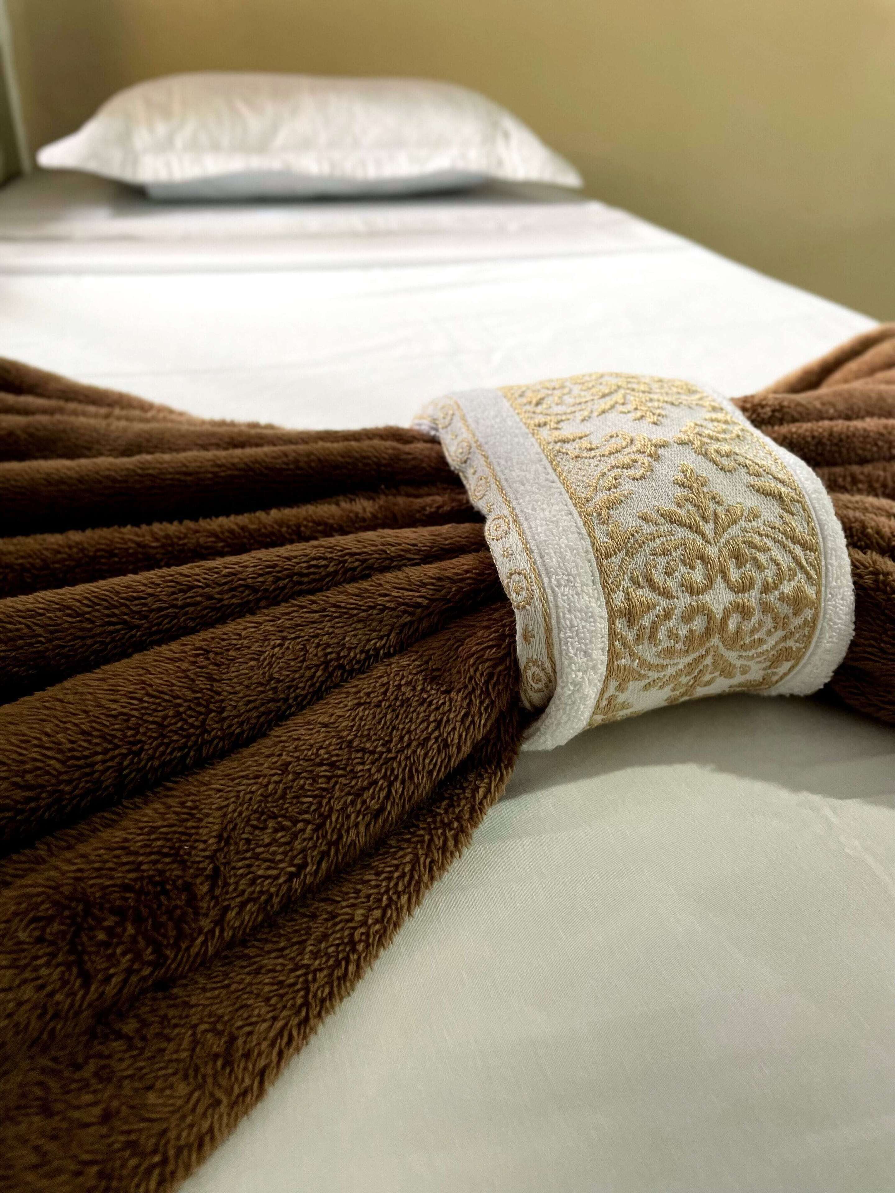 A neatly made bed with a white pillow and a brown blanket with a decorative edge.
