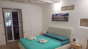 Ein Schlafzimmer mit Bett, Nachttisch, Wandlampe und einer Tür mit Blick ins Freie.