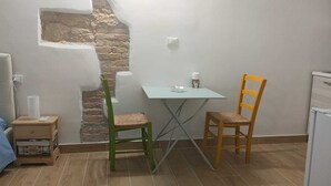 Ein kleiner Raum mit einer Steinwand, einem Tisch mit zwei Stühlen, einer kleinen Holzeinrichtung und einem weißen Kühlschrank.