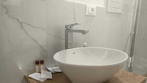 Ein Badezimmer mit einem großen, weißen Waschtisch, einer Marmorwand und einer Duschkabine.