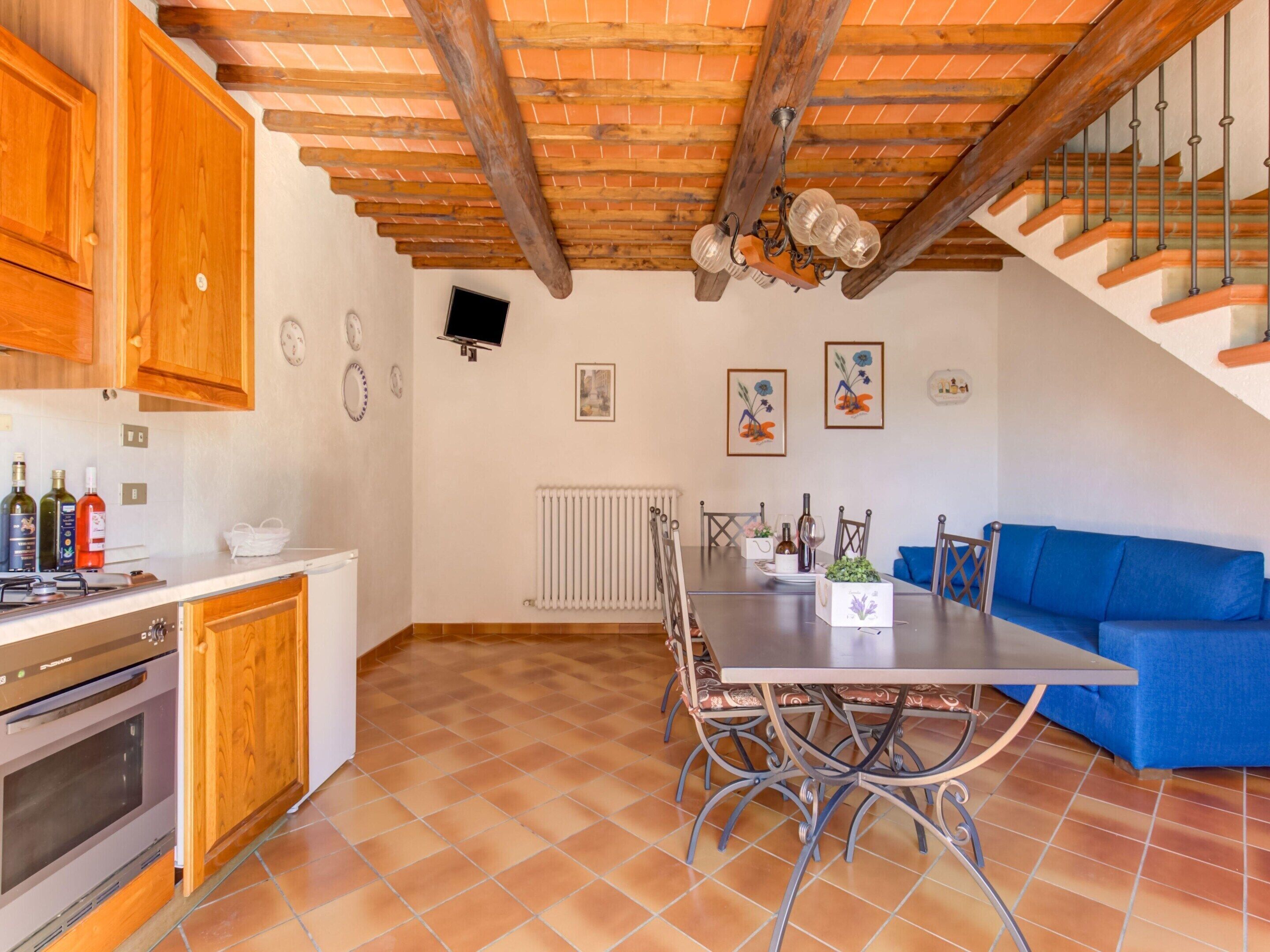 Una cocina con armarios de madera, una mesa de comedor con sillas, un sofá azul y una escalera.