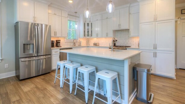 A modern kitchen with white cabinetry, stainless steel appliances, and a central island with bar stools.