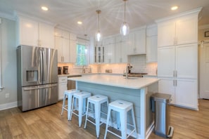 Una cocina moderna con armarios blancos, electrodomésticos de acero inoxidable y una isla central con taburetes de bar.