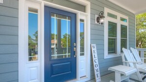 A house with a blue front door, a 'WELCOME' sign, and two white Adirondack chairs on the porch.