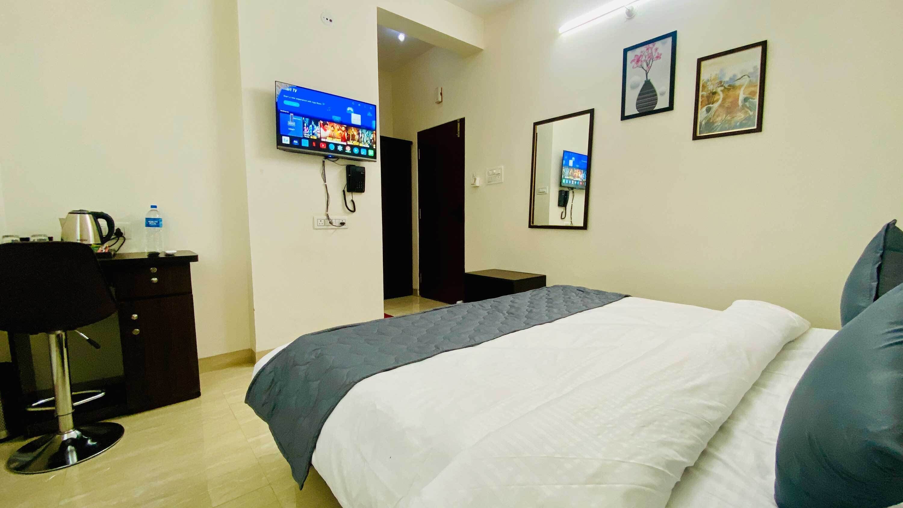 Een hotelkamer met een bed, een bureau met een waterkoker, een televisie en een spiegel.