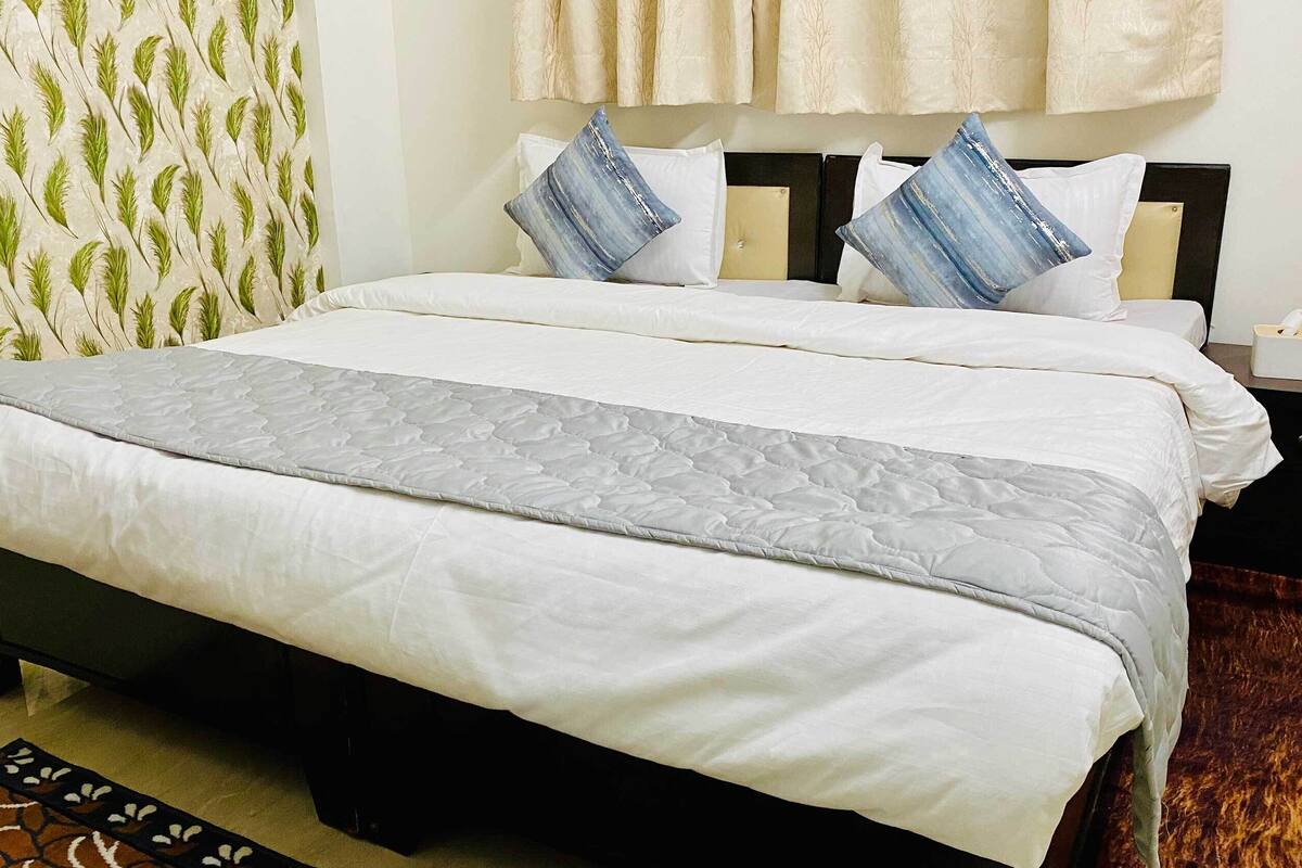 A bed with a grey quilt, white pillows, and a blue accent pillow.