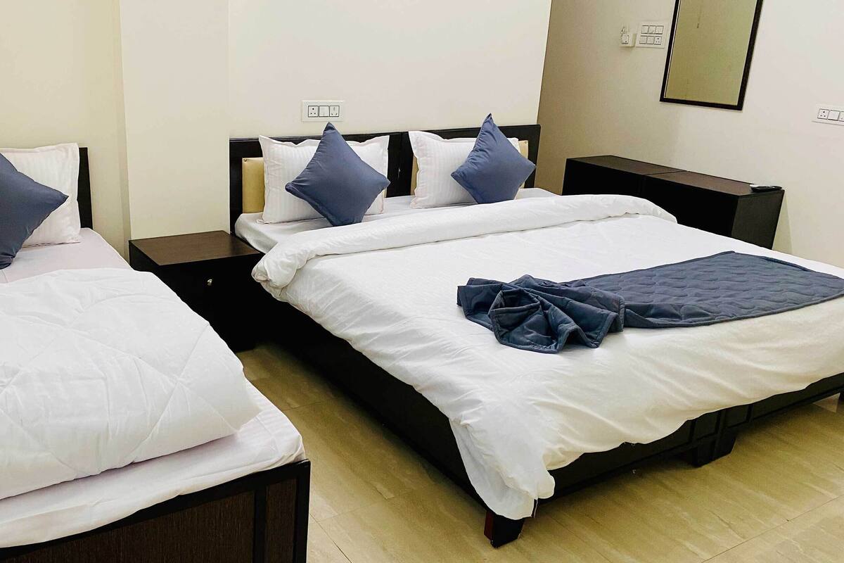 A hotel room with two beds, each with white bedding and dark blue pillows. There is a wooden nightstand with a remote control on it.
