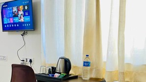 Une chambre d’hôtel équipée d’un bureau, d’une chaise, d’un téléviseur fixé au mur, d’une bouteille d’eau et d’une bouilloire.