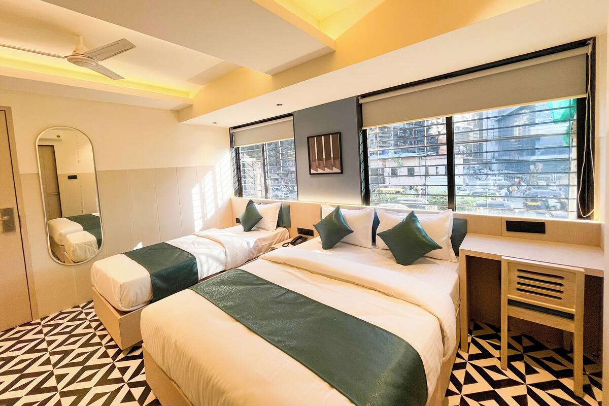 A hotel room with two beds, a large mirror, a ceiling fan, and a view of the city through the windows.