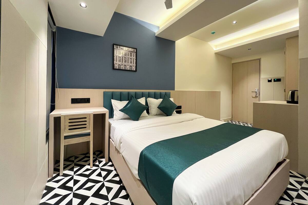 A modern hotel room with a bed, bedside table, and a small seating area.