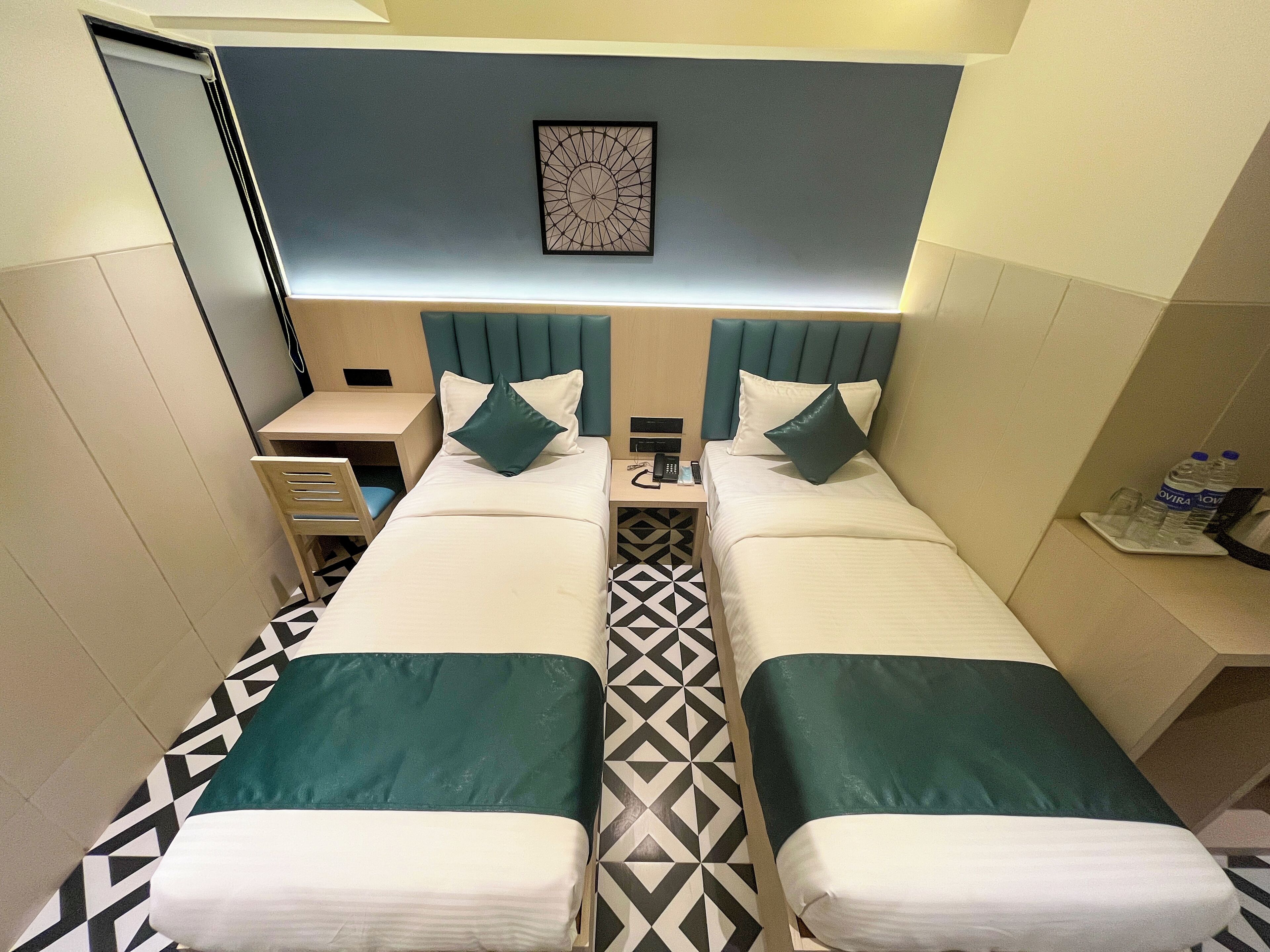 A hotel room with two beds, a desk, a chair, a bedside table, a phone, and a water bottle.