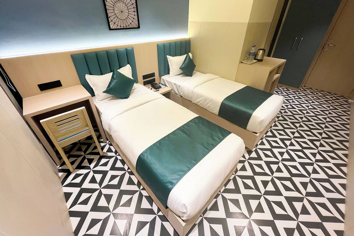 A hotel room with two beds, a nightstand, a desk, and a patterned floor.