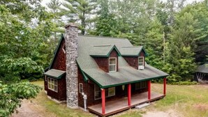 Een rustieke chalet met een stenen schoorsteen, een groen dak en een veranda met rode leuningen.