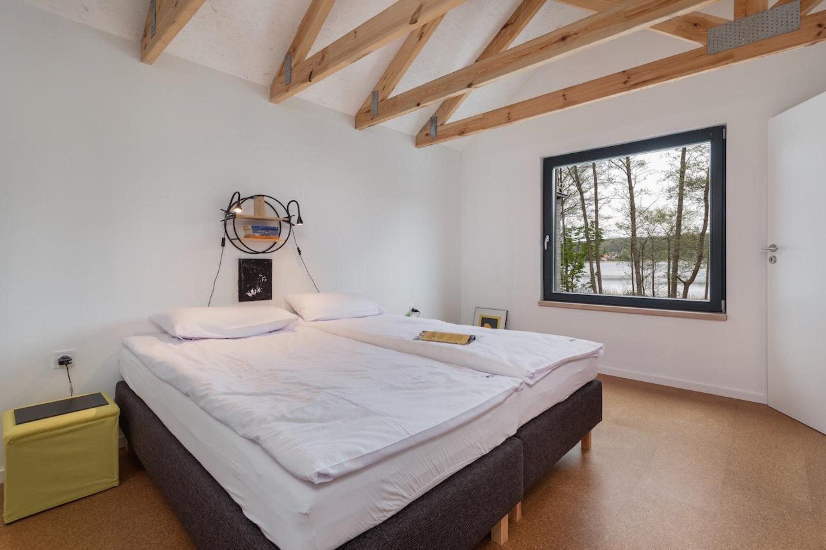 Een slaapkamer met een groot bed, een raam met uitzicht op bomen en een houten plafond.