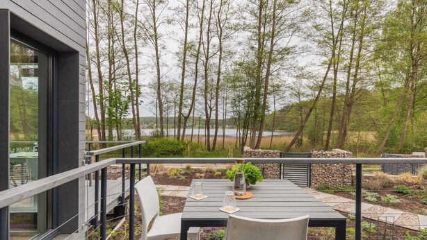 Eine Terrasse mit Tisch und Stühlen mit Blick auf einen See, umgeben von Bäumen.