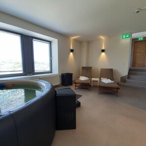 Un espace détente avec un jacuzzi, deux chaises en bois, une petite table et un escalier.