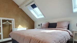 A bedroom with a sloped ceiling, a skylight, a bed with a pink and gray duvet, a white wardrobe, and a bedside table. - Luxury Family Holiday Home With Wellness (Weiswampach)