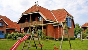 A residential house with a red-tiled roof, a wooden swing set, and a red slide in the yard. - Ferienresort in Fehmarn-lemkenhafen (Fehmarn)