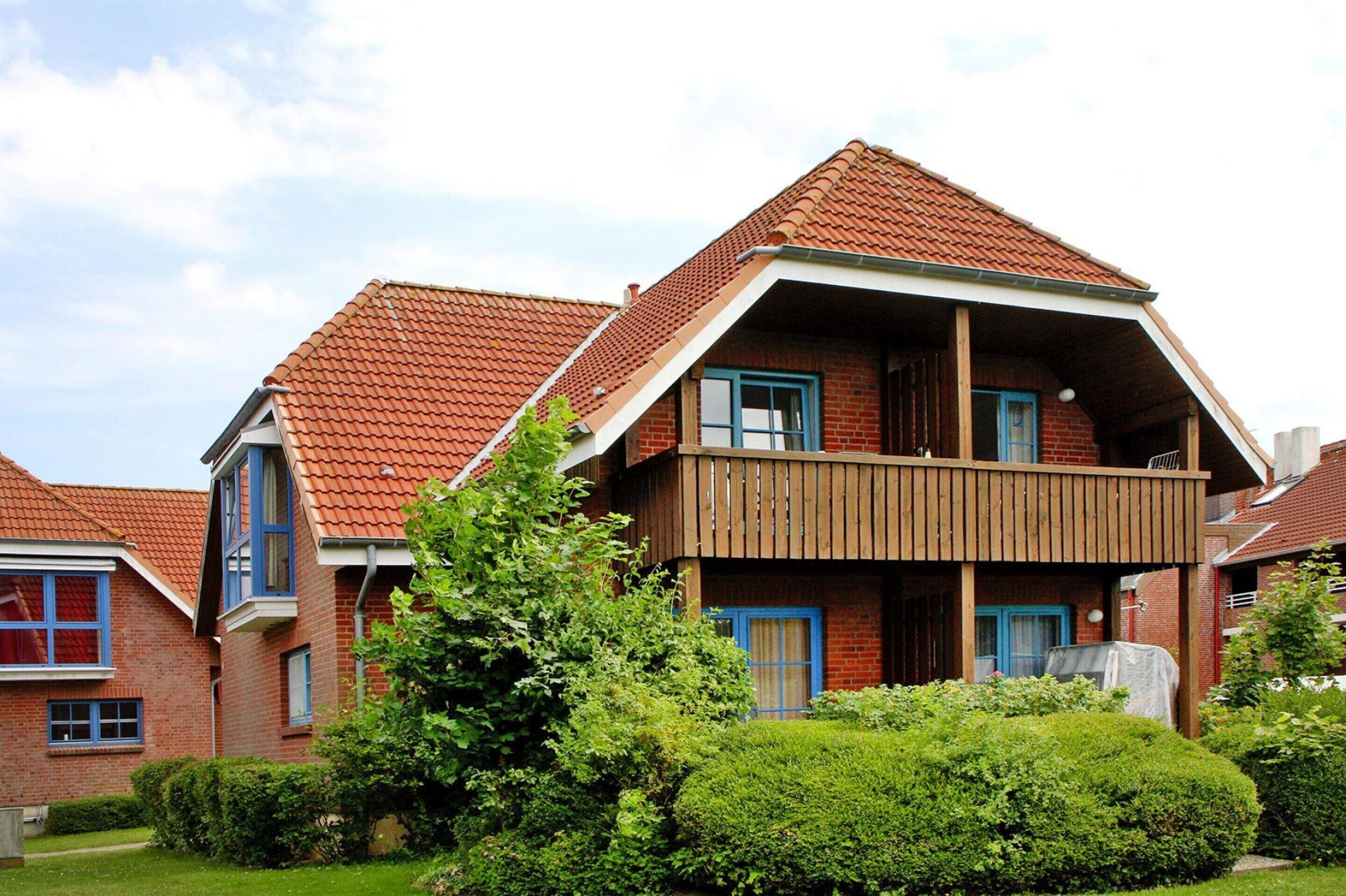 A two-story brick house with a red-tiled roof, a wooden balcony, and a well-maintained garden.
