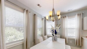 A dining room with a large white table, white curtains, and a chandelier.