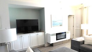A modern living room with a flat-screen TV, a fireplace, grey sofas, and a white cabinet.