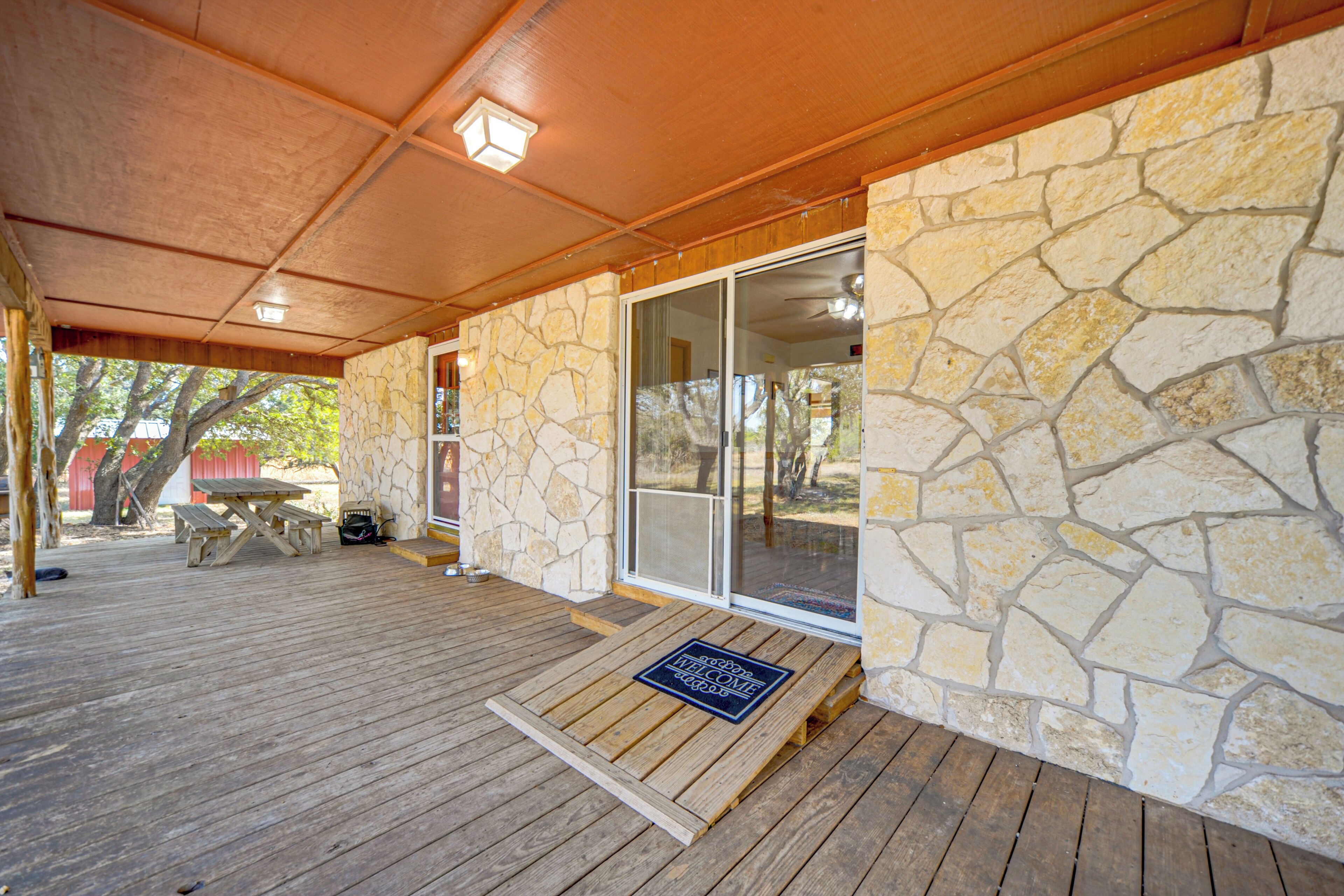 A covered patio area with a stone wall, a wooden deck, and a sliding glass door leading to a covered outdoor space.