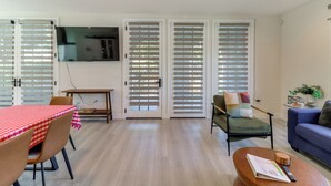 Ein Wohnzimmer mit Essbereich, einer Couch, einem an der Wand montierten Fernseher und einem Tisch mit rotem Karotisch.
