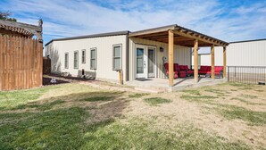 A single-story house with a covered patio area, a fenced yard, and a wooden deck. - Fenced Yard: Modern Barndominium in Amarillo! (Amarillo)
