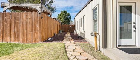 A backyard with a stone pathway leading to a wooden fence and a white building with a door.