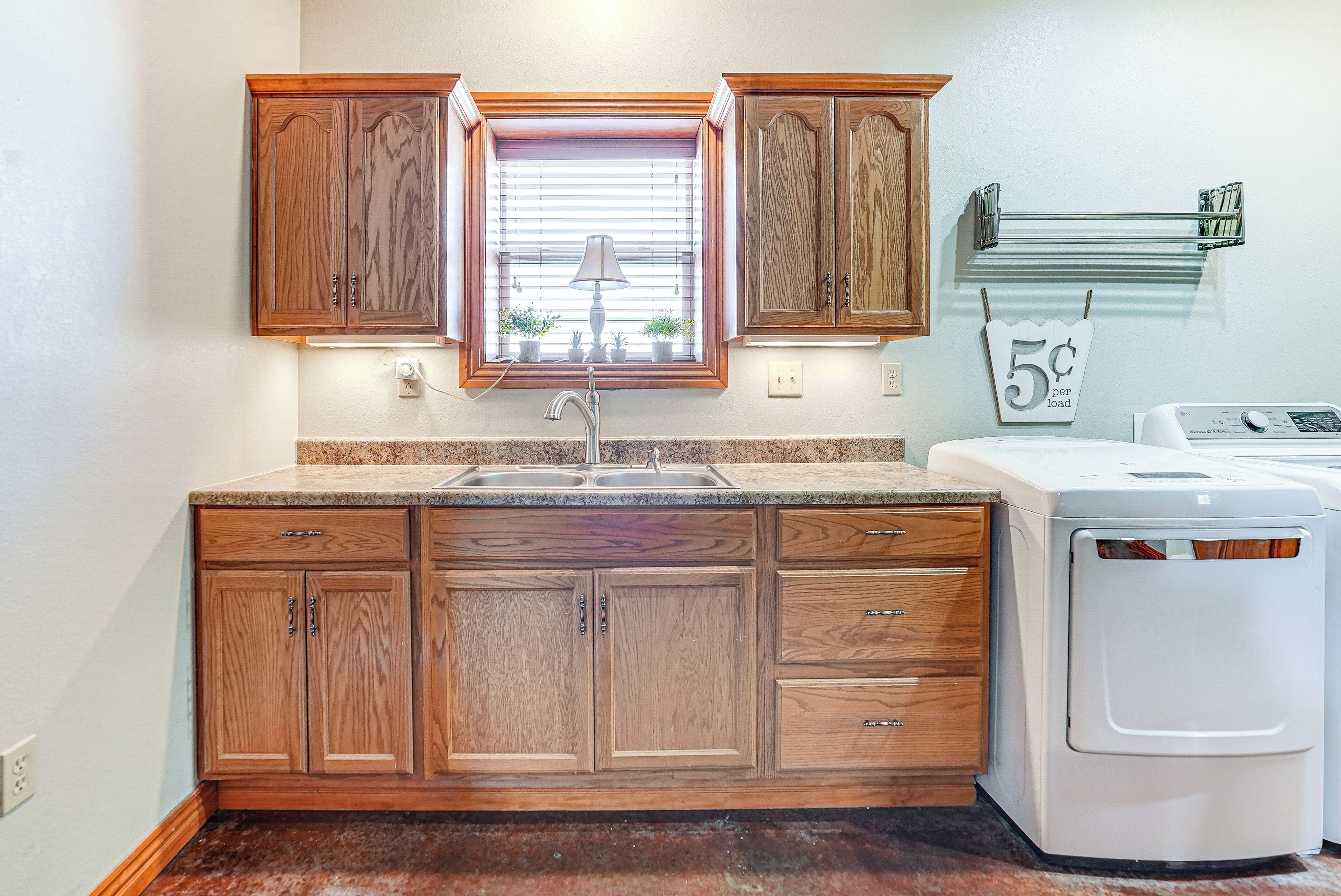 A kitchen with wooden cabinets, a window with blinds, a sink, a washing machine, and a towel rack with a price tag.