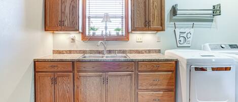 A kitchen with wooden cabinets, a window with blinds, a sink, a washing machine, and a towel rack with a price tag.