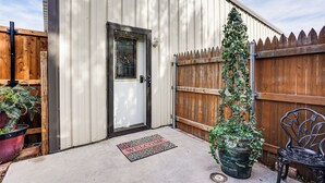 A metal building with a door, a welcome mat, a wooden fence, a potted plant, and a metal chair. - Fenced Yard: Modern Barndominium in Amarillo! (Amarillo)
