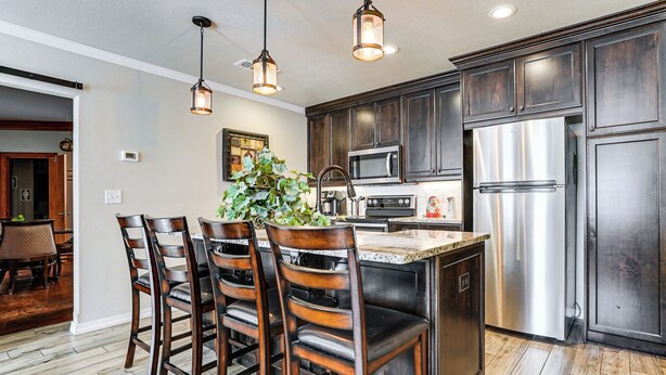 A modern kitchen with dark wooden cabinets, stainless steel appliances, and a central island with bar stools. - Fenced Yard: Modern Barndominium in Amarillo! (Amarillo)