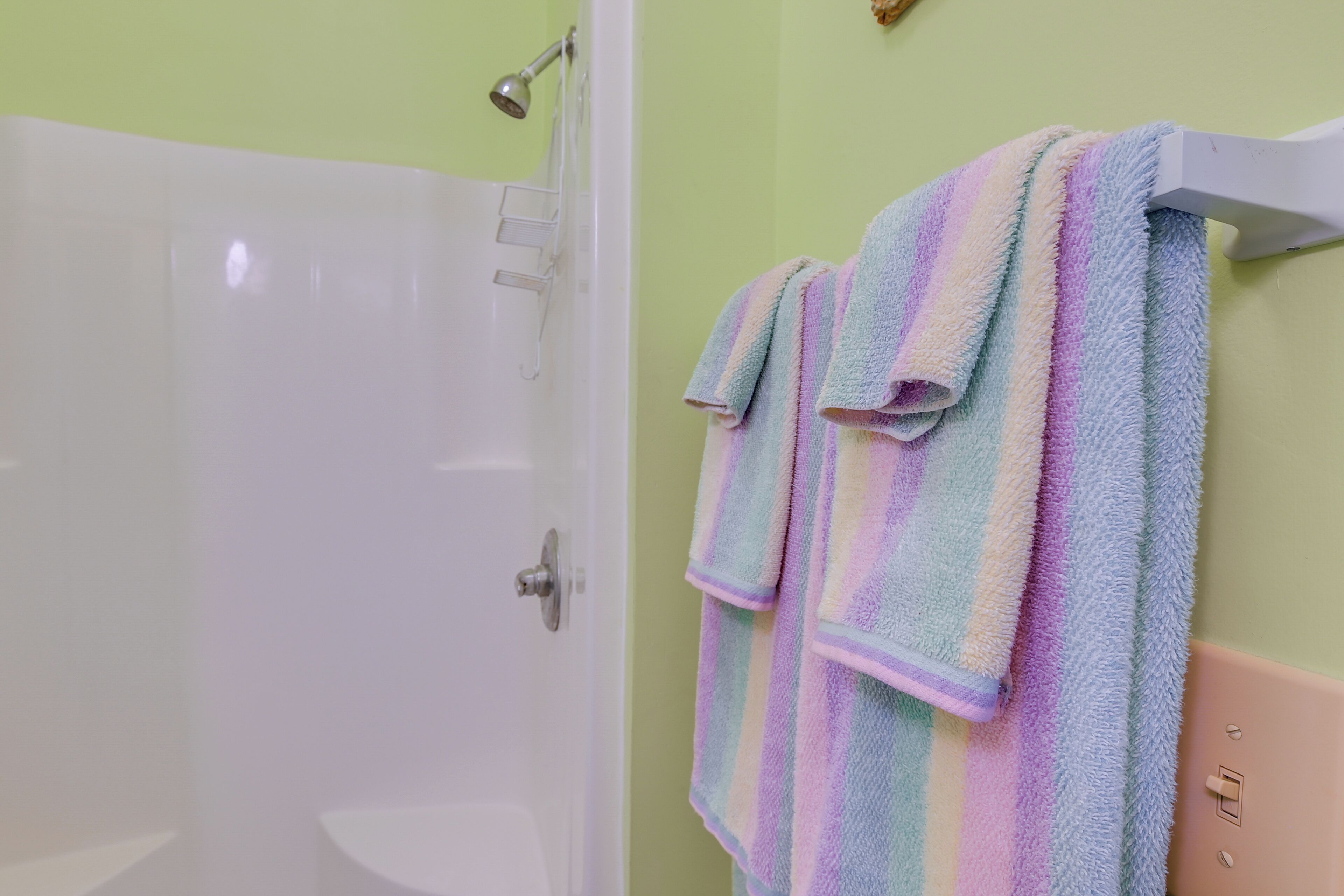 A bathroom with a shower, a white bathtub, and a towel rack with striped towels.