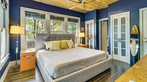 Un dormitorio con una cama grande, suelo de madera, ventilador de techo y una ventana con persianas.
