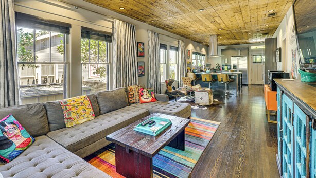 Un amplio salón con techo de madera, un sofá grande con cojines de colores, y una cocina al fondo.