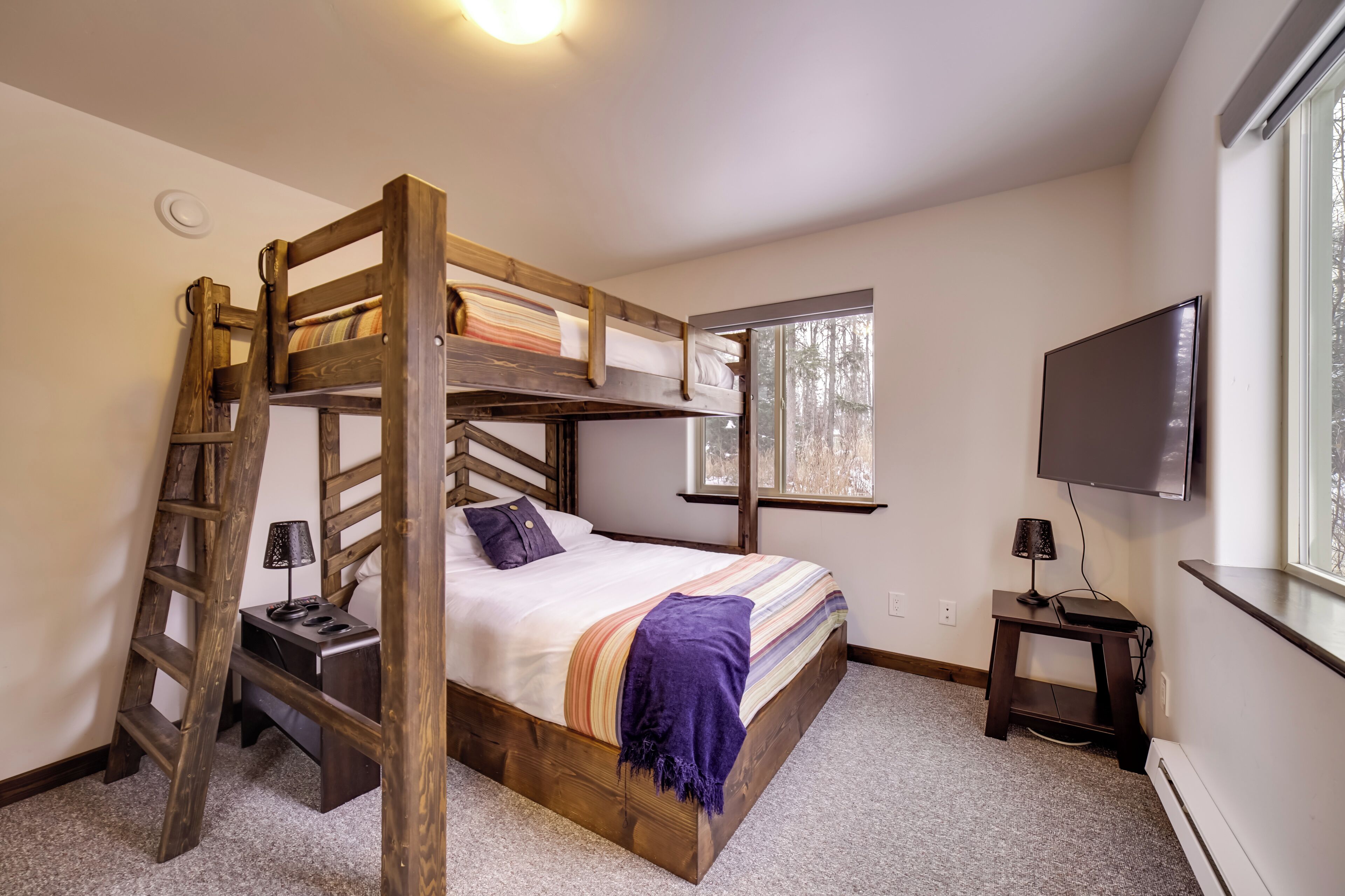 A bunk bed room with a ladder, a desk, a chair, and a TV.