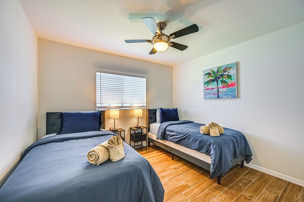 A bedroom with two beds, a ceiling fan, a window with blinds, and a painting on the wall. - Patio, Dock + Canal Access: Cape Coral Home! (Cape Coral)