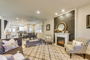 A spacious living room with a fireplace, patterned armchairs, and a dining area in the background. - 6 Mi to Downtown - Spacious Home in Pittsburgh! (Pittsburgh)