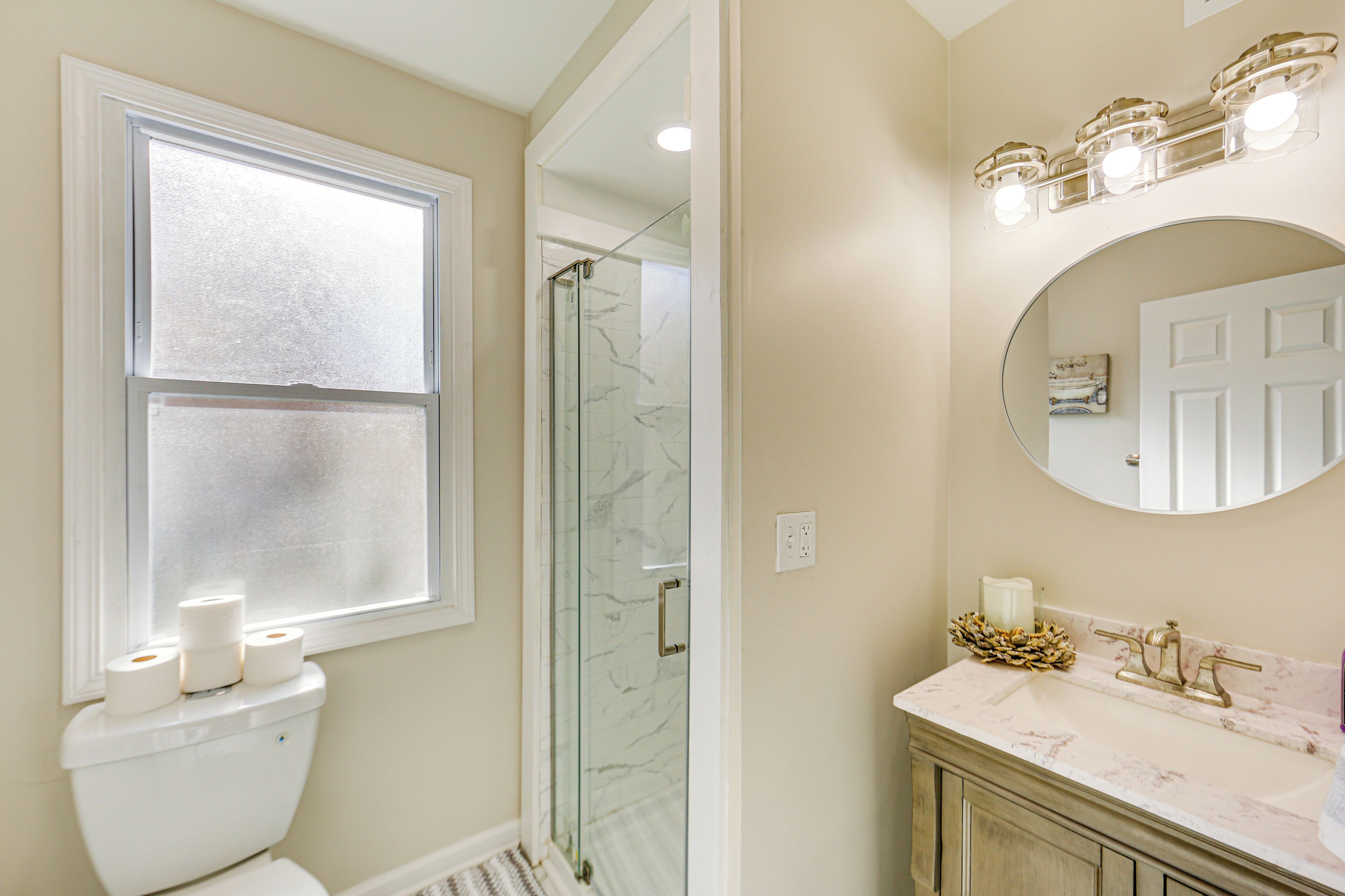 A bathroom with a toilet, a glass shower enclosure, a sink with a marble countertop, and a mirror above the sink.