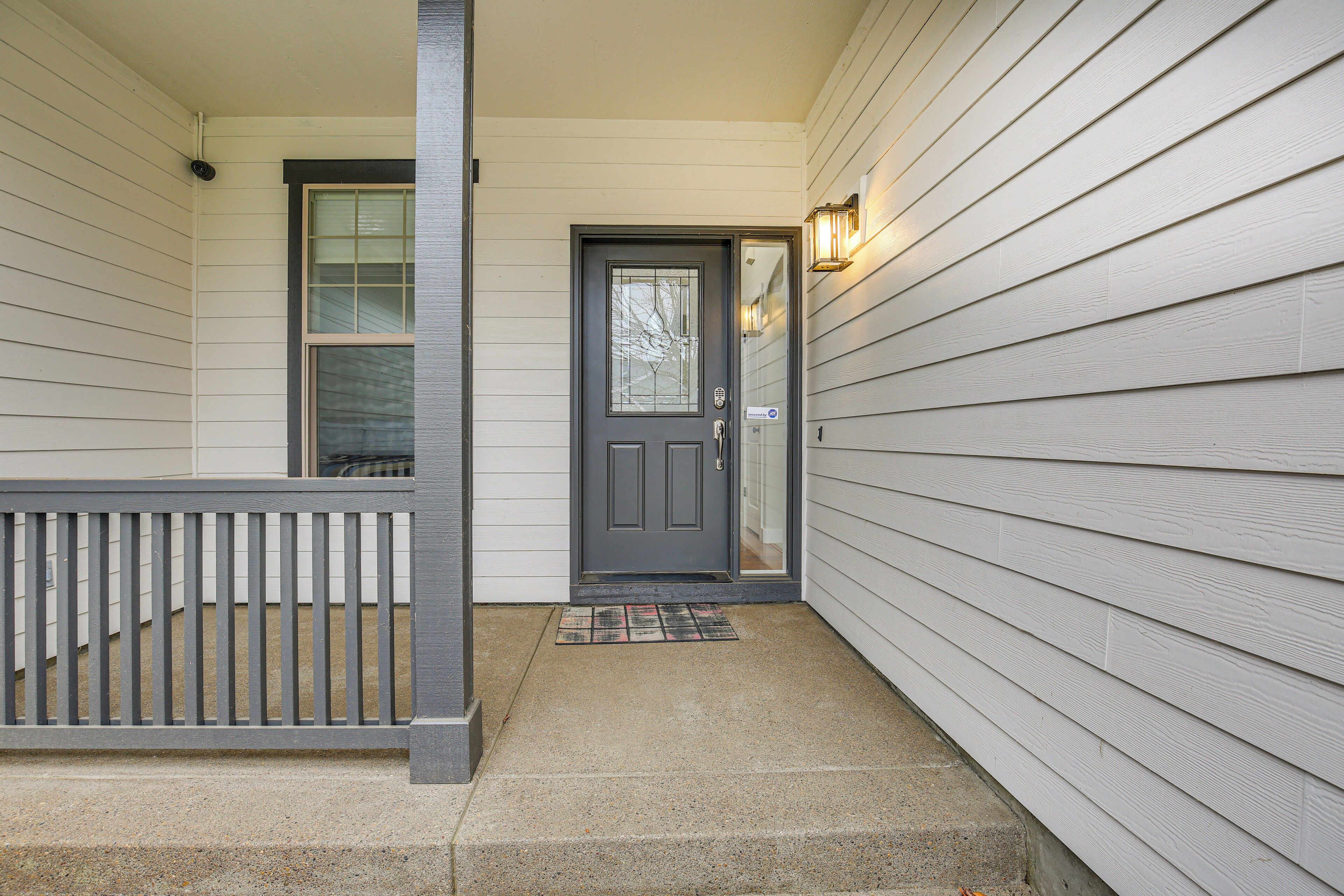 A front porch with a dark gray door, a small step leading up to it, and a light fixture on the wall to the right.