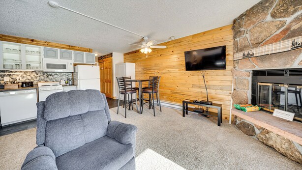 A modern living room with a grey sofa, a stone fireplace, a flat-screen TV mounted on the wall, and a wooden dining area. - 2 Mi to Granby Ranch: Mtn-view Studio w/ Perks (Granby)