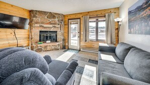 A cozy living room with a stone fireplace, wooden walls, and a large gray sofa. - 2 Mi to Granby Ranch: Mtn-view Studio w/ Perks (Granby)