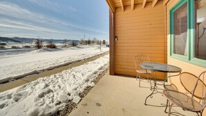 A wooden building with a covered patio area featuring a metal table and chairs, a view of a snowy landscape, and a clear sky. - 2 Mi to Granby Ranch: Mtn-view Studio w/ Perks (Granby)