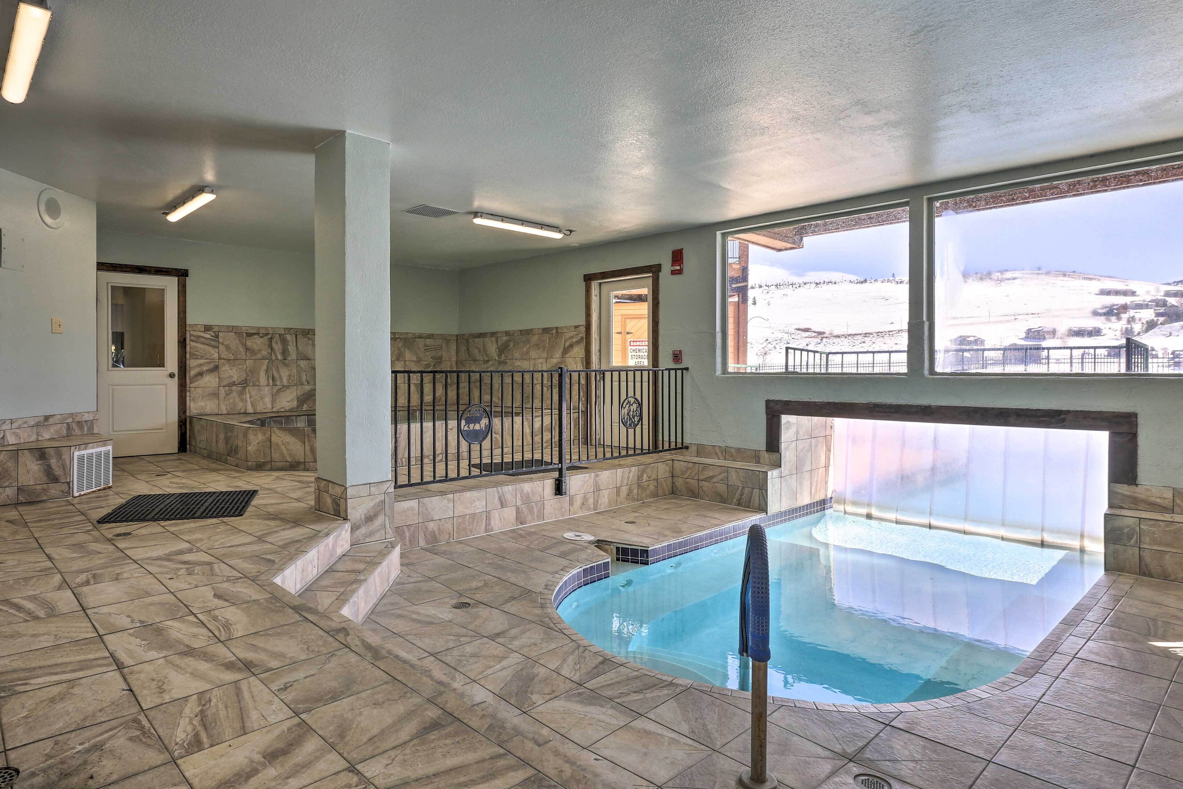 An indoor swimming pool with a view of a snowy landscape through large windows.