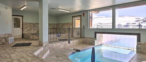 An indoor swimming pool with a view of a snowy landscape through large windows.
