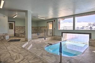 An indoor swimming pool with a view of a snowy landscape through large windows.